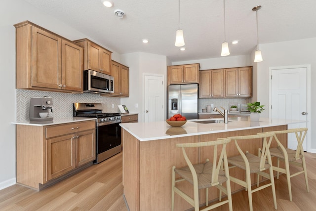 kitchen featuring a sink, appliances with stainless steel finishes, a breakfast bar area, and light wood finished floors