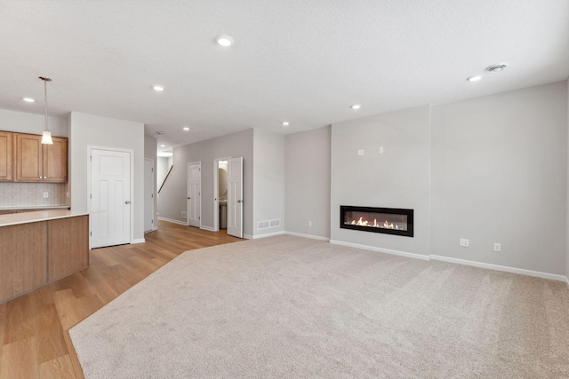 unfurnished living room with light wood-type flooring, visible vents, a glass covered fireplace, recessed lighting, and baseboards