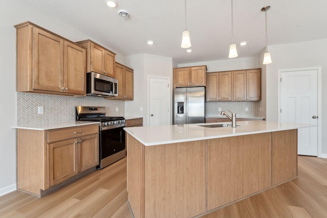 kitchen with light wood finished floors, a kitchen island with sink, a sink, appliances with stainless steel finishes, and light countertops