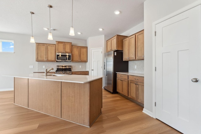 kitchen featuring brown cabinetry, light wood finished floors, a sink, stainless steel appliances, and light countertops