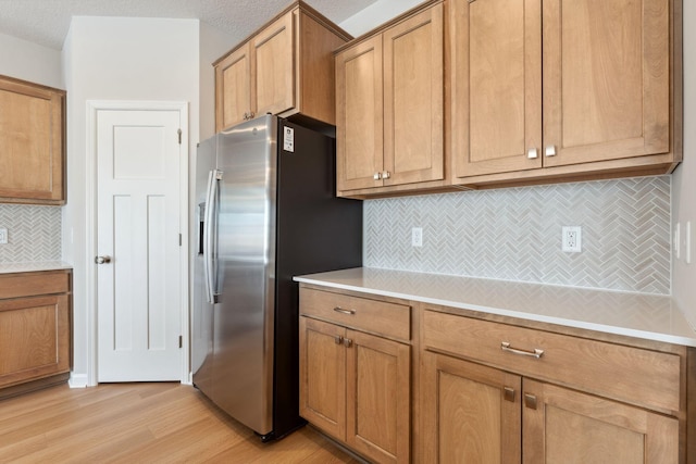 kitchen featuring light countertops, light wood-style flooring, tasteful backsplash, and stainless steel refrigerator with ice dispenser