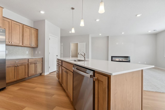 kitchen featuring a sink, decorative backsplash, stainless steel appliances, a glass covered fireplace, and brown cabinets