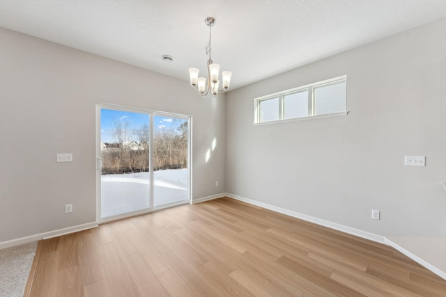 empty room featuring a notable chandelier, light wood-type flooring, and baseboards