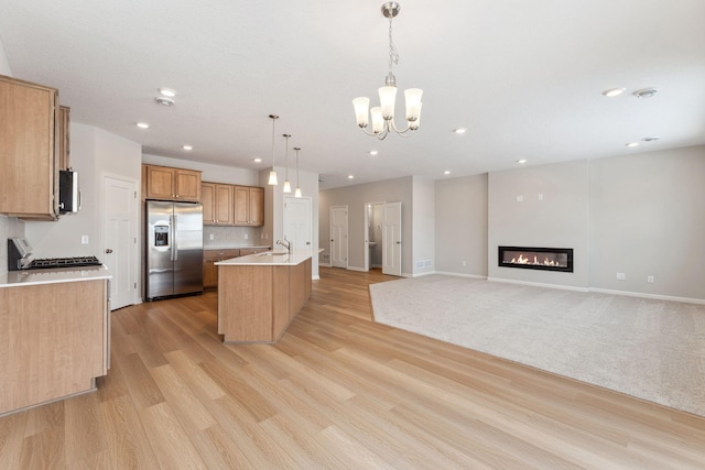 kitchen featuring a center island with sink, light wood-style floors, stainless steel refrigerator with ice dispenser, stove, and a glass covered fireplace