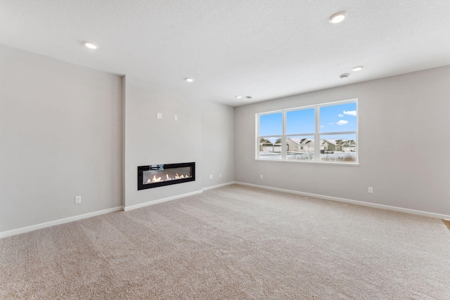 unfurnished living room with a glass covered fireplace, recessed lighting, carpet, and baseboards