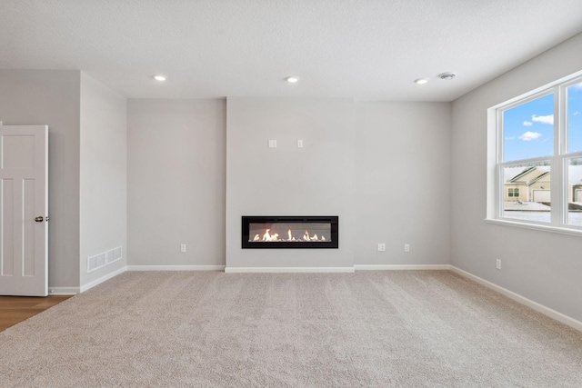 unfurnished living room featuring carpet, baseboards, visible vents, recessed lighting, and a glass covered fireplace