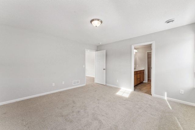 unfurnished bedroom featuring ensuite bath, light colored carpet, visible vents, and baseboards