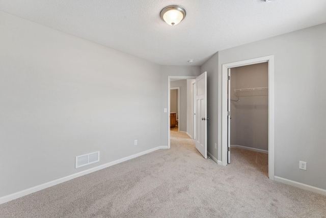 unfurnished bedroom with visible vents, a walk in closet, a closet, baseboards, and light colored carpet