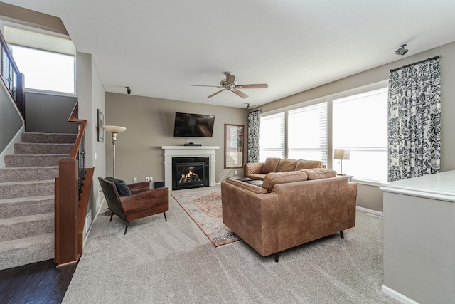 carpeted living room with stairs, a glass covered fireplace, baseboards, and ceiling fan