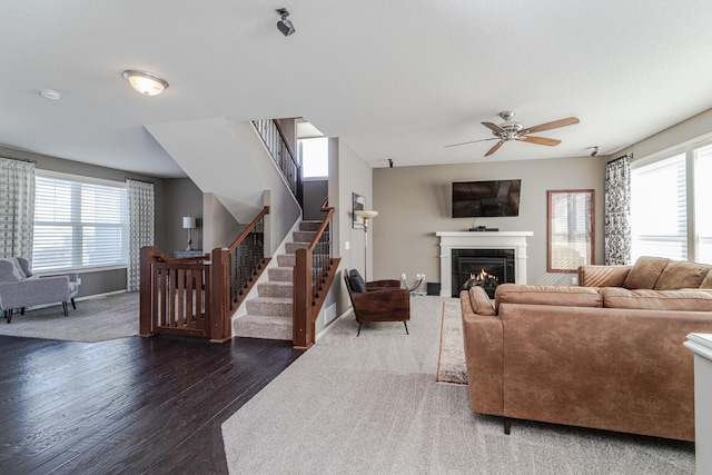 living room featuring wood finished floors, a glass covered fireplace, stairway, baseboards, and ceiling fan