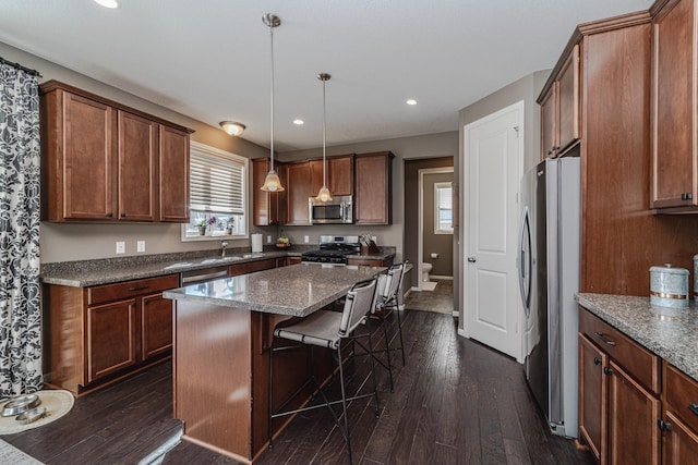 kitchen featuring a sink, a center island, stainless steel appliances, dark stone counters, and dark wood-style flooring