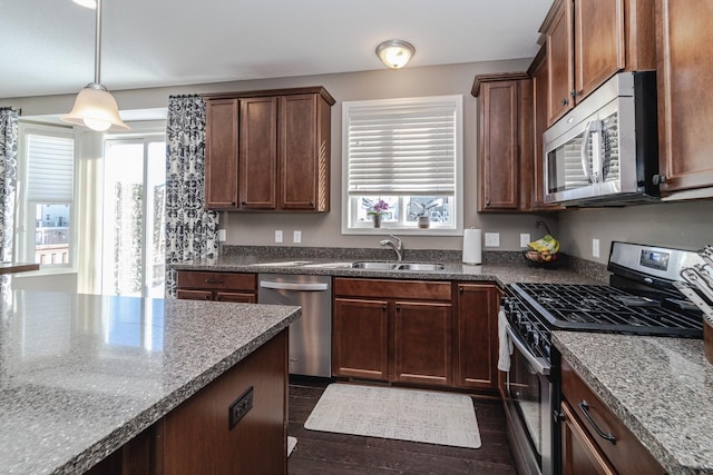 kitchen with a sink, dark stone countertops, hanging light fixtures, and stainless steel appliances