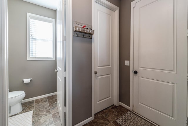 bathroom featuring toilet, baseboards, and stone finish flooring