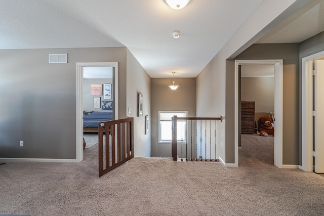 hall with visible vents, an upstairs landing, carpet, and baseboards