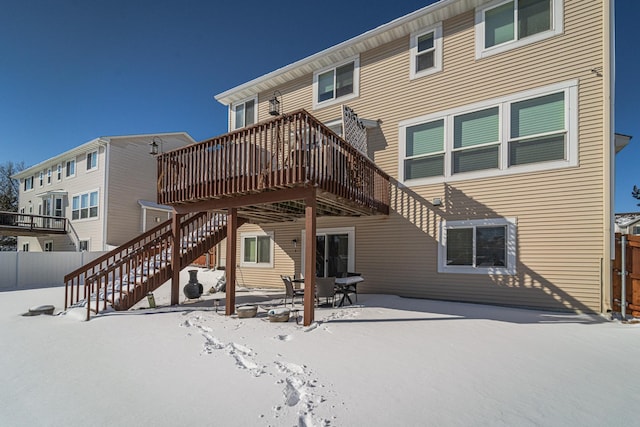 snow covered house featuring stairway, a wooden deck, a patio, and fence