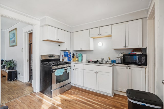 kitchen with crown molding, black microwave, light wood-style flooring, stainless steel gas stove, and a sink