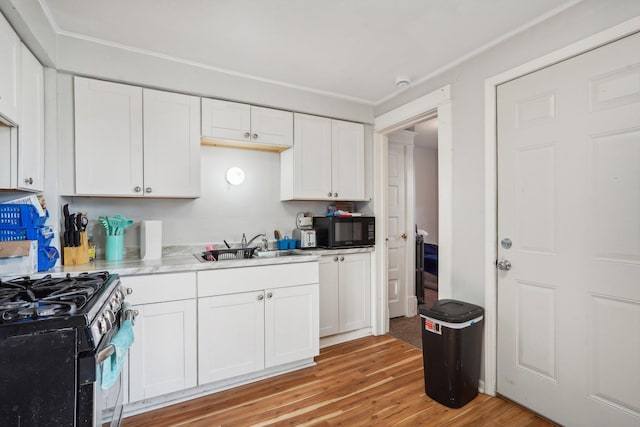 kitchen featuring black microwave, light countertops, range with gas stovetop, light wood-style floors, and a sink