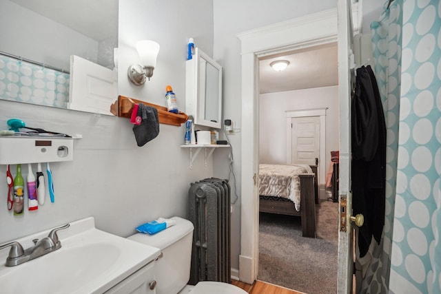 ensuite bathroom with toilet, ensuite bathroom, a sink, curtained shower, and radiator heating unit