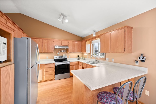 kitchen featuring light countertops, vaulted ceiling, appliances with stainless steel finishes, a peninsula, and a sink