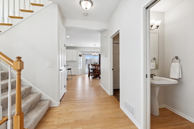 corridor with light wood finished floors, visible vents, stairs, and baseboards