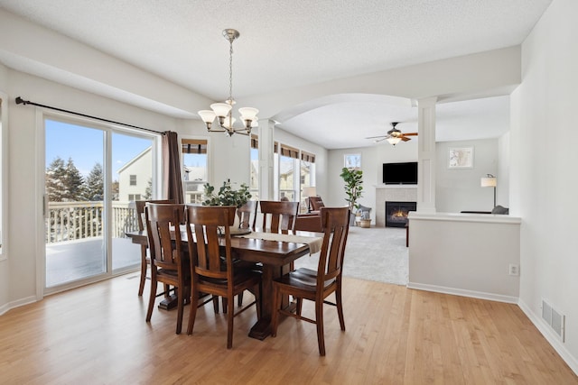 dining room featuring visible vents, a tiled fireplace, ceiling fan with notable chandelier, a textured ceiling, and light wood-style floors