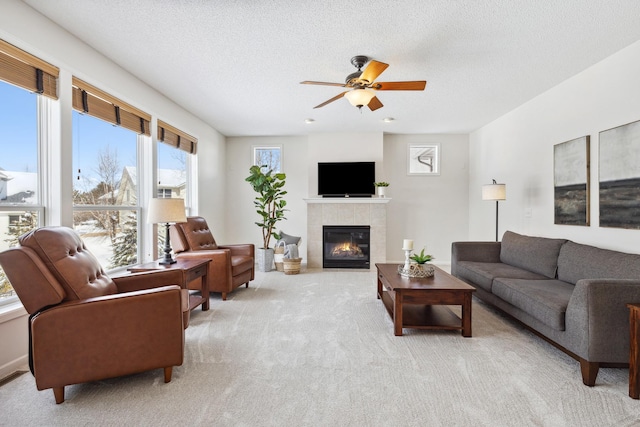 living area with light colored carpet, ceiling fan, a tiled fireplace, and a textured ceiling