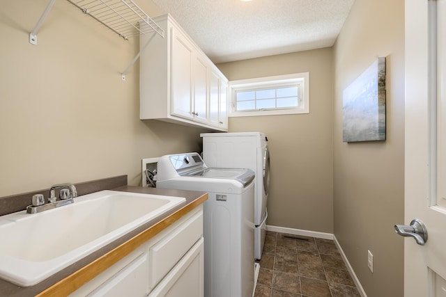 washroom with baseboards, washing machine and clothes dryer, cabinet space, a sink, and a textured ceiling