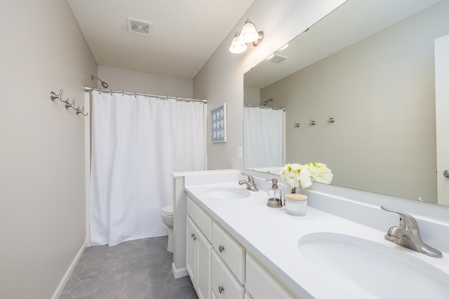 bathroom featuring double vanity, toilet, visible vents, and a sink