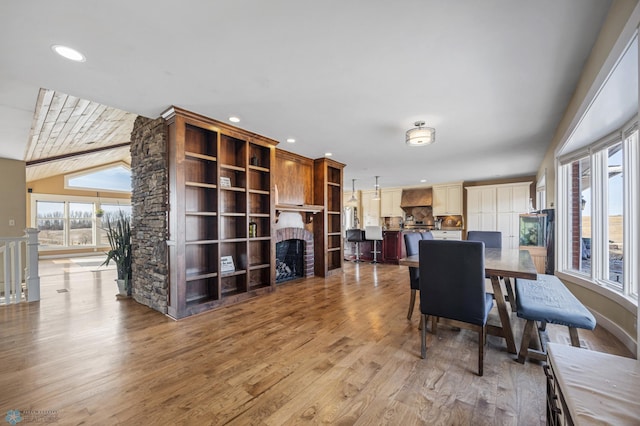 dining room featuring lofted ceiling, recessed lighting, a fireplace, and light wood-type flooring