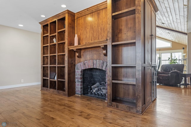 unfurnished living room featuring lofted ceiling, a brick fireplace, wood finished floors, and baseboards