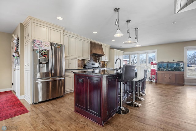 kitchen featuring custom exhaust hood, cream cabinetry, stainless steel appliances, and wood finished floors