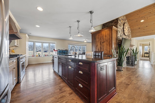 kitchen with stainless steel range with gas cooktop, a center island with sink, recessed lighting, wood finished floors, and a sink