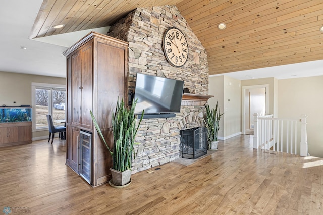 living area featuring wood ceiling, high vaulted ceiling, a stone fireplace, and wood finished floors