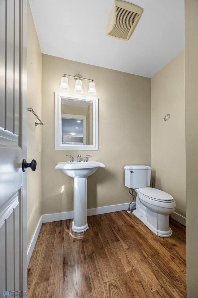 bathroom with visible vents, baseboards, toilet, wood finished floors, and a sink