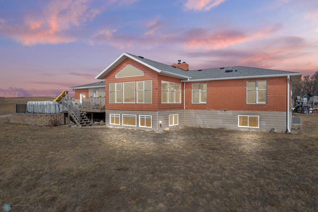 rear view of property featuring brick siding, a shingled roof, a wooden deck, stairs, and a lawn