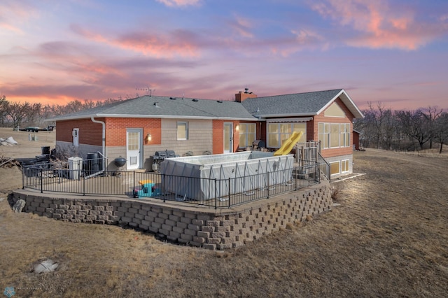 back of property at dusk featuring a patio area, a chimney, and a shingled roof