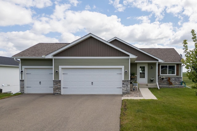 craftsman-style house with a front yard, an attached garage, a shingled roof, stone siding, and aphalt driveway