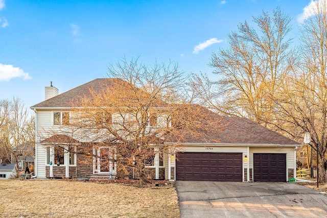 view of front facade featuring a shingled roof, a garage, driveway, and a chimney