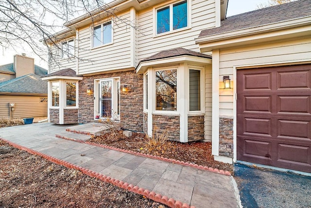 entrance to property with an attached garage, stone siding, and roof with shingles