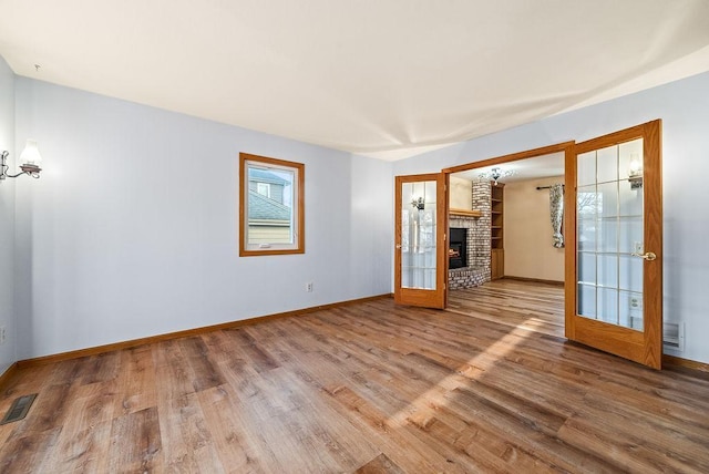 spare room featuring wood finished floors, visible vents, baseboards, french doors, and a brick fireplace