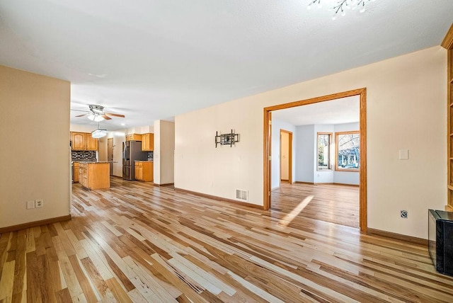 unfurnished living room with light wood-type flooring, visible vents, baseboards, and a ceiling fan