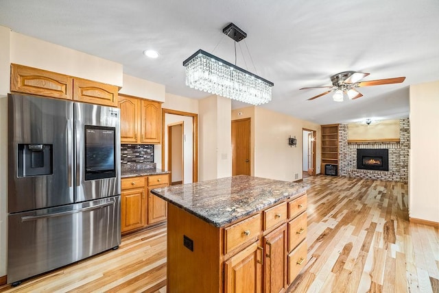 kitchen with dark stone countertops, light wood-type flooring, stainless steel fridge, and a fireplace