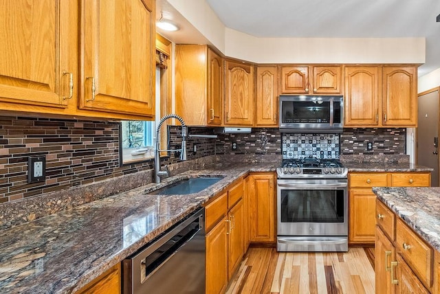 kitchen featuring brown cabinets, stainless steel appliances, light wood-type flooring, and a sink