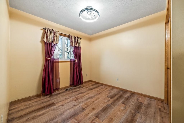 unfurnished room featuring visible vents, baseboards, a textured ceiling, and wood finished floors