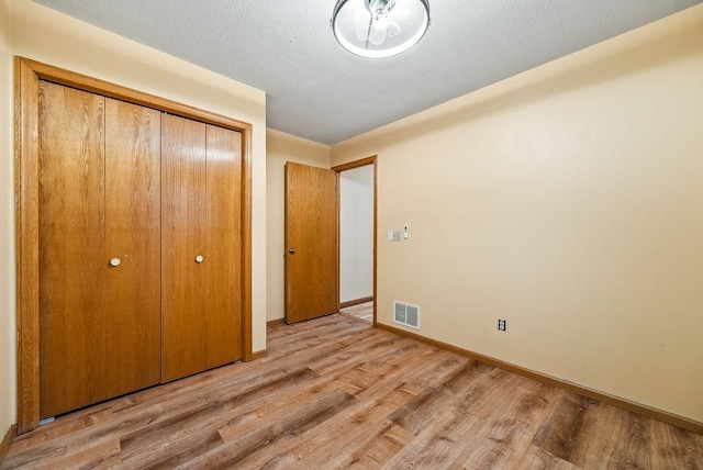 unfurnished bedroom with visible vents, a textured ceiling, a closet, light wood finished floors, and baseboards