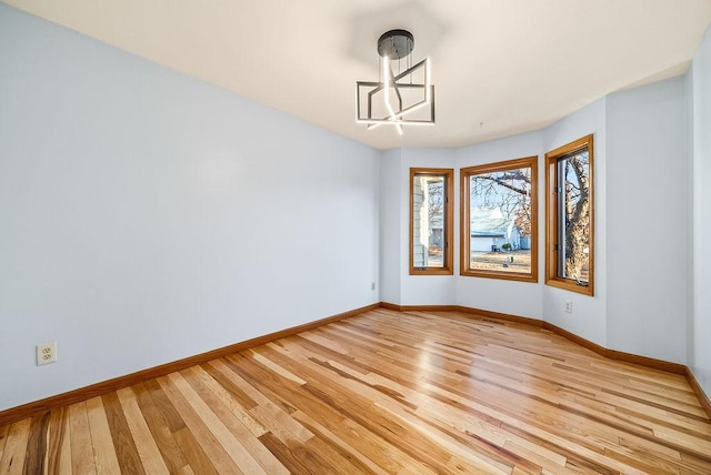 unfurnished room with baseboards, an inviting chandelier, and light wood finished floors