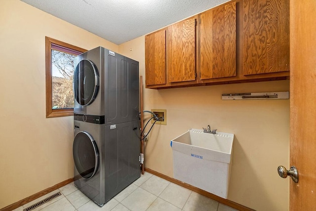 laundry room with visible vents, a textured ceiling, stacked washing maching and dryer, cabinet space, and light tile patterned floors