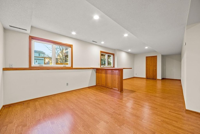 empty room with plenty of natural light, light wood-style floors, and a textured ceiling