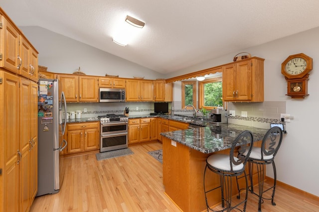 kitchen featuring vaulted ceiling, light wood-style flooring, appliances with stainless steel finishes, a peninsula, and a sink