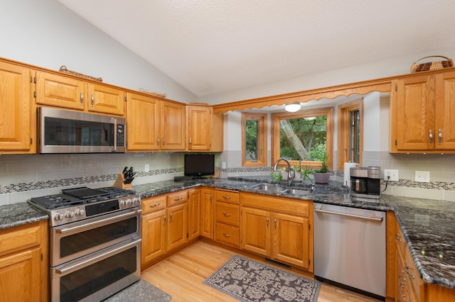 kitchen featuring a sink, tasteful backsplash, stainless steel appliances, light wood finished floors, and lofted ceiling